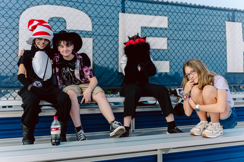 A group of people in costumes sitting on bleachers, with a soda bottle nearby.