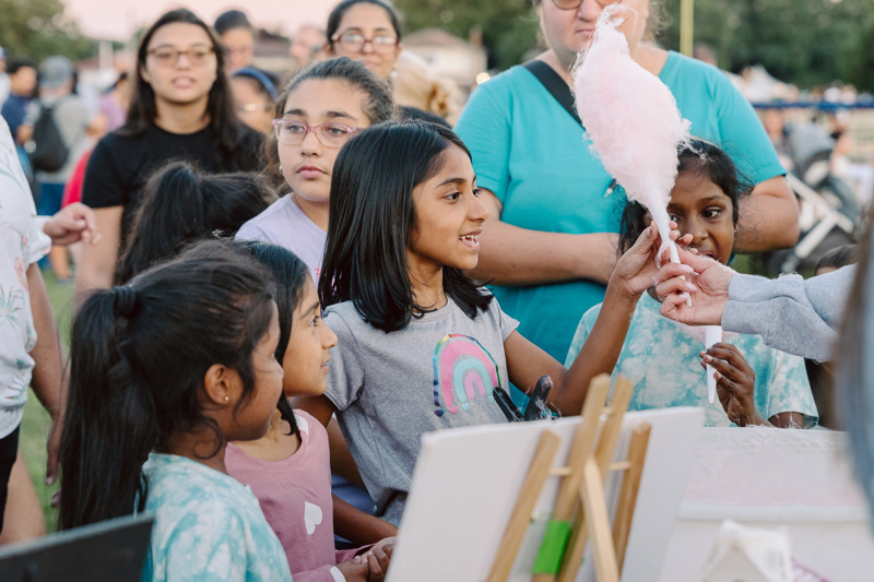 A group of people at an outdoor event watching a person holding cotton candy.