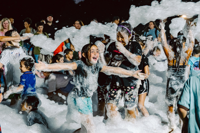 A group of people playing in foam at an outdoor event during nighttime.
