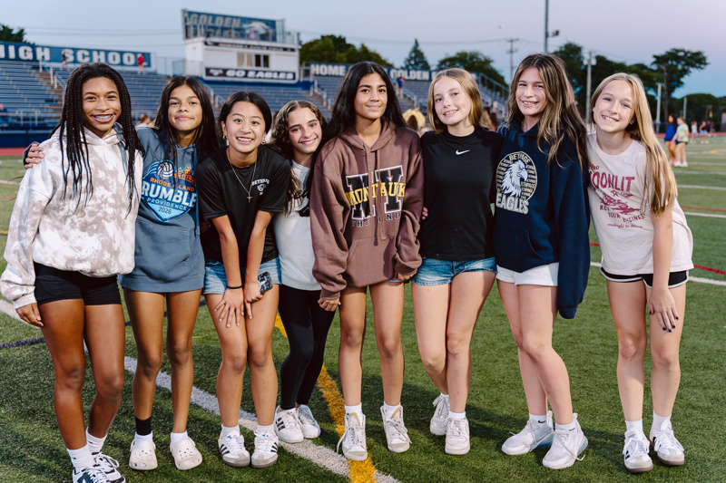 A group of people standing together on a sports field in front of bleachers.