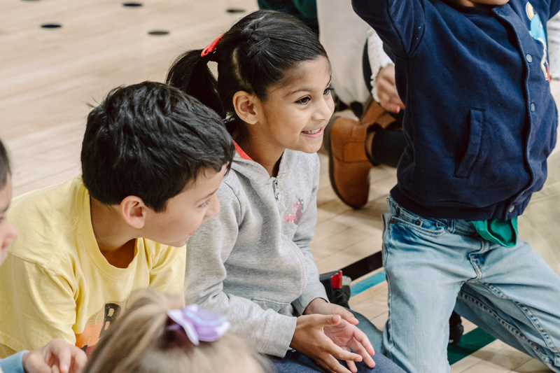 A group of children sitting on a floor, with a person in the background.