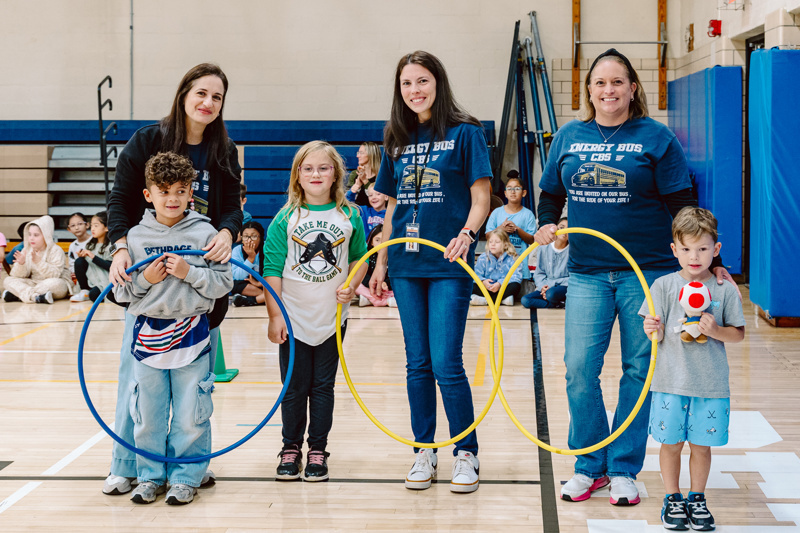 people interact with a hula hoop in a gym while students watch.