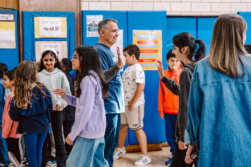 People interacting in a school gym with blue walls and educational posters displayed.