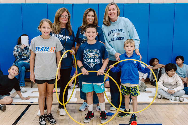people interact with a hula hoop in a gym while students watch.