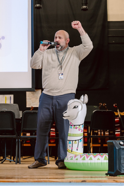 A person speaks into a microphone during a school event in an indoor setting.