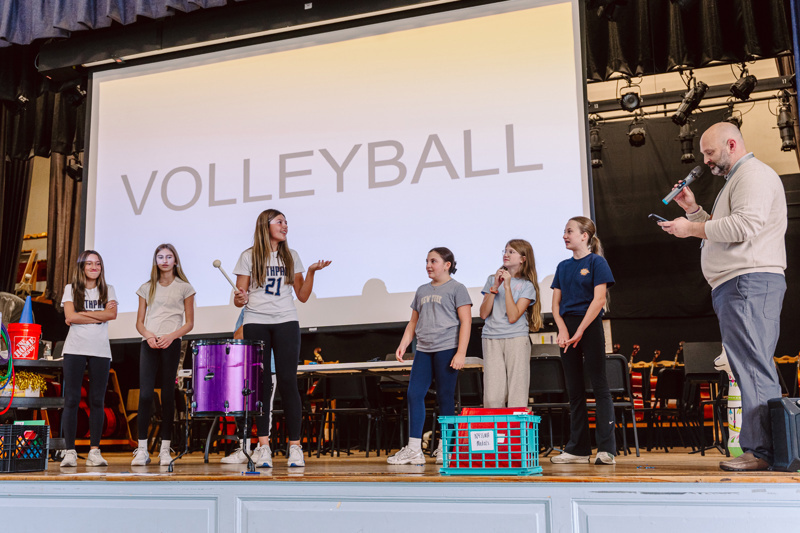 A group stands on stage with a volleyball theme backdrop during a presentation or event.