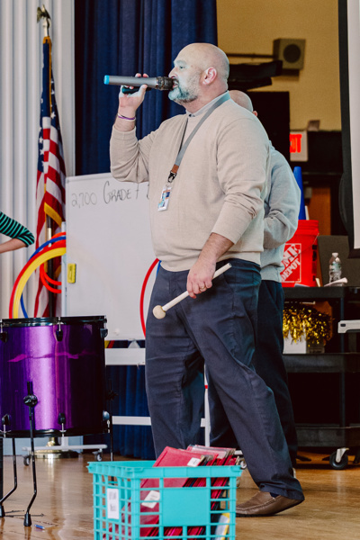 A person speaks into a microphone during a school event in an indoor setting.