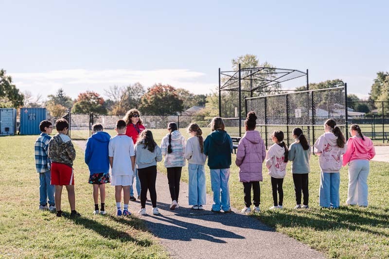 Students listening to teacher speak on playground.