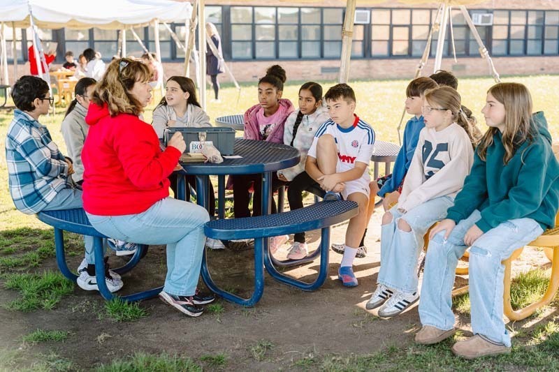 Students sitting with teacher outside.