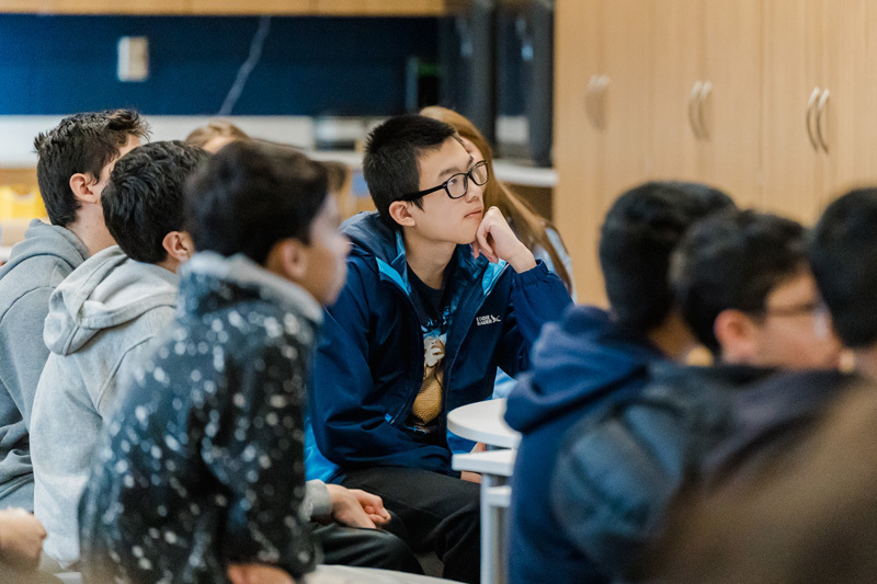 A classroom scene where attentive students in casual clothing are seated, focusing on a lecture. The atmosphere is contemplative and curious.