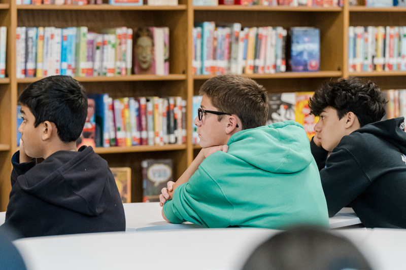 A classroom scene where attentive students in casual clothing are seated, focusing on a lecture. The atmosphere is contemplative and curious.