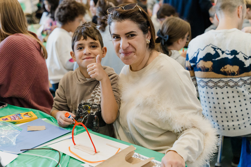 students are crafting at a table. They are focused on a paper project. The scene is lively, conveying creativity and concentration.