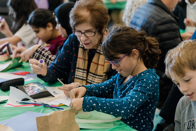 students are crafting at a table. They are focused on a paper project. The scene is lively, conveying creativity and concentration.