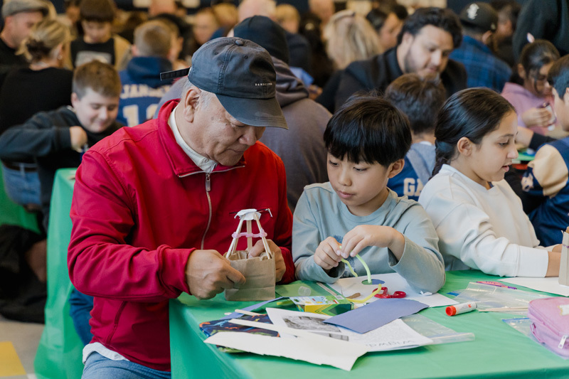 students are crafting at a table. They are focused on a paper project. The scene is lively, conveying creativity and concentration.