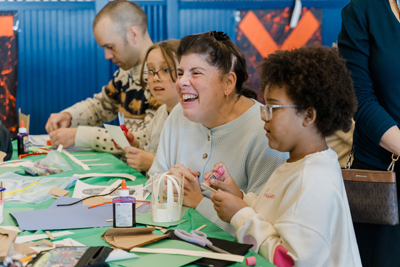 students are crafting at a table. They are focused on a paper project. The scene is lively, conveying creativity and concentration.