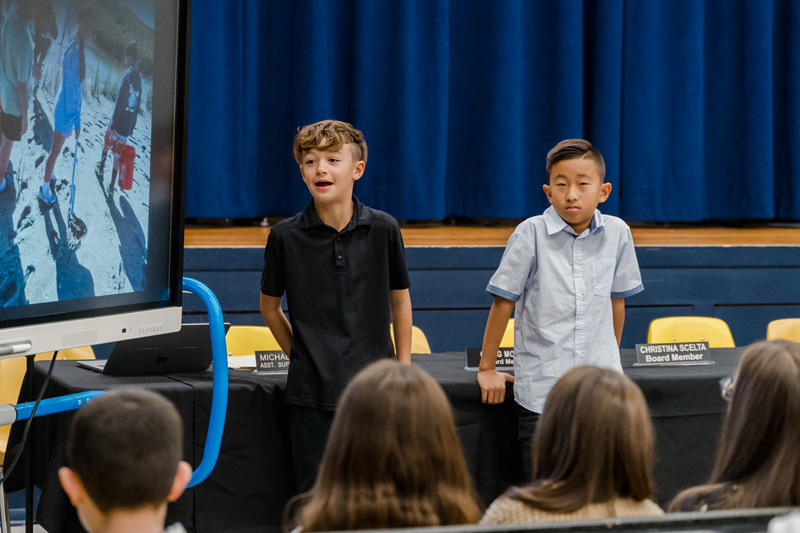 students present confidently in front of an audience, standing by a screen 
