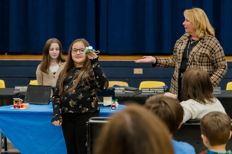 students present confidently in front of an audience, standing by a screen 