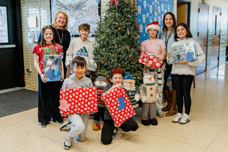 people pose with gifts by tree