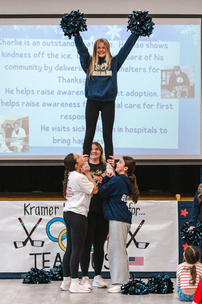A diverse group of children sit closely together, some waving small American flags. A boy in a red shirt is smiling brightly, creating a joyful, patriotic atmosphere.