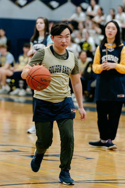 players wearing a “Golden Eagles” jerseyplaying basketball on a gym court, focused and determined. Blurred spectators watch in the background.