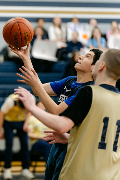 players wearing a “Golden Eagles” jerseyplaying basketball on a gym court, focused and determined. Blurred spectators watch in the background.
