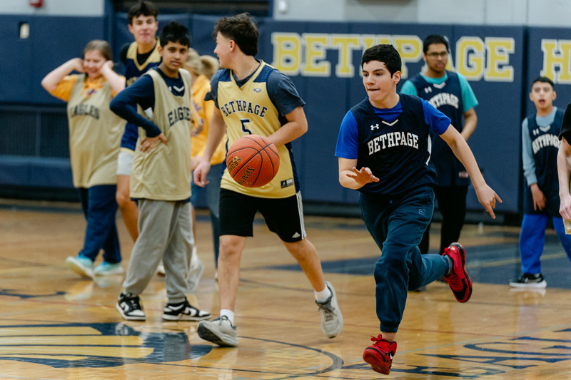 players wearing a “Golden Eagles” jerseyplaying basketball on a gym court, focused and determined. Blurred spectators watch in the background.