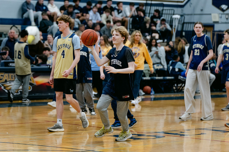 players wearing a “Golden Eagles” jerseyplaying basketball on a gym court, focused and determined. Blurred spectators watch in the background.