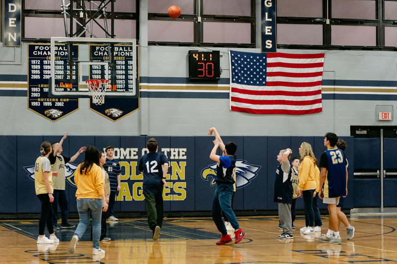 players wearing a “Golden Eagles” jerseyplaying basketball on a gym court, focused and determined. Blurred spectators watch in the background.
