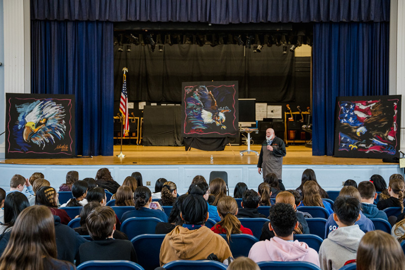 A group of students sits attentively at lab tables in a auditorium