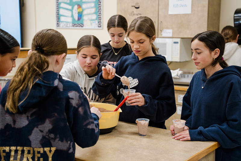 A group of students sits attentively at lab tables in a classroom, 