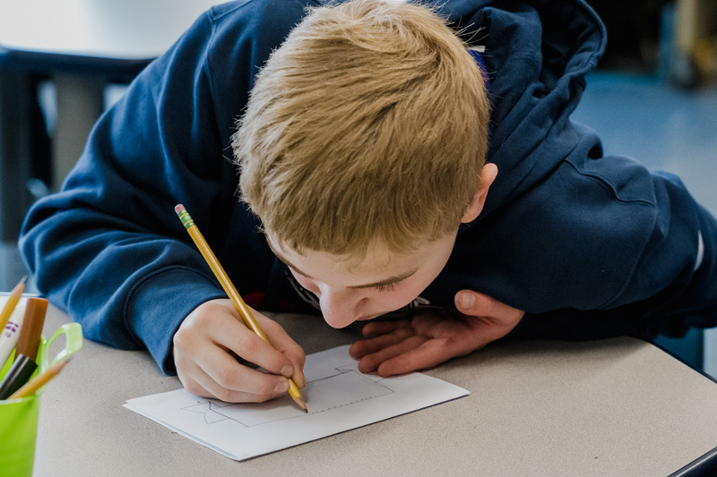 student focused on drawing with a pencil on white paper