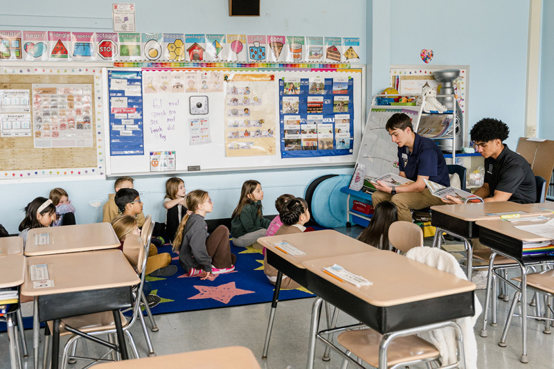 people read books to seated children in a classroom.