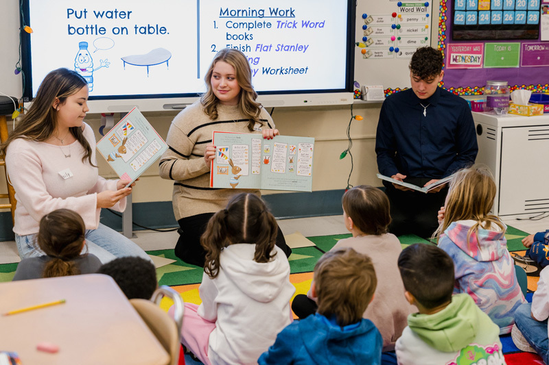 people read books to seated children in a classroom.