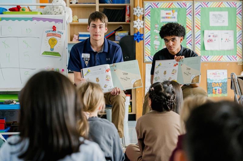 people read books to seated children in a classroom.