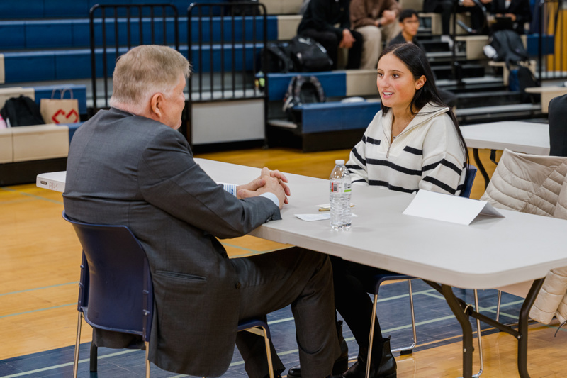 A job fair in a gymnasium with pairs of people engaged in discussions at numbered table