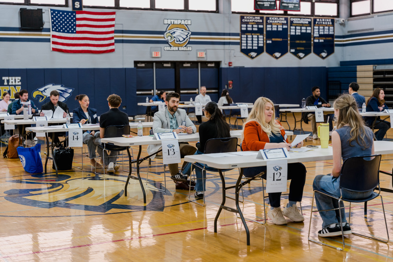 A job fair in a gymnasium with pairs of people engaged in discussions at numbered table