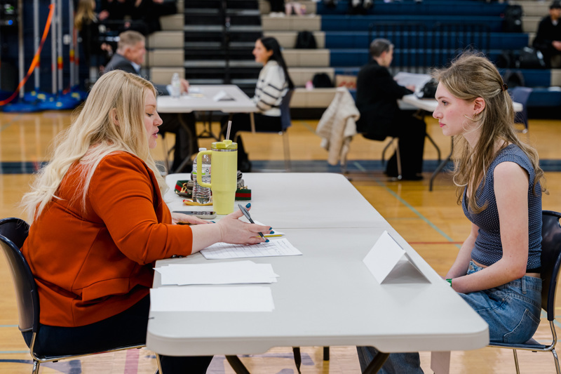 A job fair in a gymnasium with pairs of people engaged in discussions at numbered table