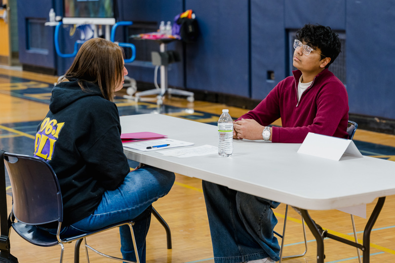 A job fair in a gymnasium with pairs of people engaged in discussions at numbered table