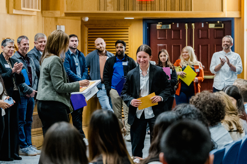 A diverse group of professionals, dressed in business attire, stand on stage