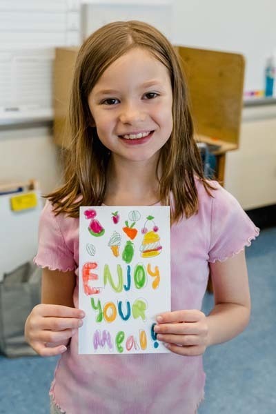 Student proudly holding artwork.
