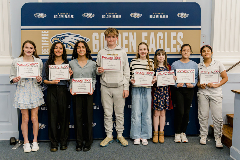 Group of students proudly holding certificates of recognition in front of the Bethpage Golden Eagles backdrop at an award ceremony.