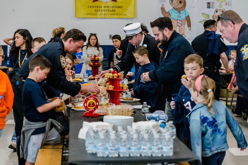Community event at Central Boulevard Elementary with children and firefighters enjoying a meal together, fostering relationships and celebration.