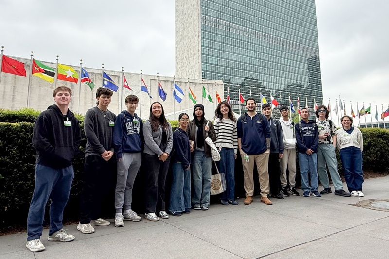 Group of students and educators posing in front of a colorful mural depicting diverse individuals, highlighting themes of community and support.