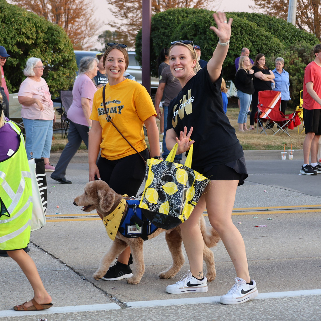 Two teacher from Grant Wood Elementary with Chico the therapy dog smiling and waving