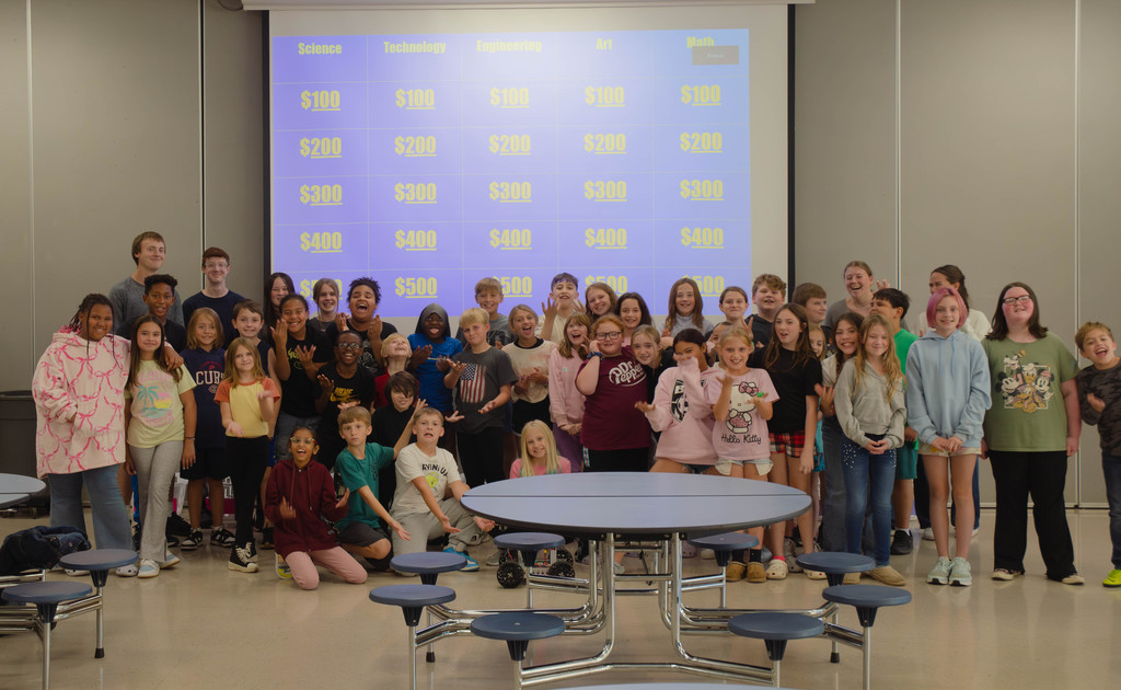 Elementary students in front of their Jeopardy wall