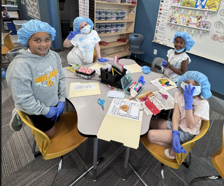 Students posing for a picture in surgical gear while disecting text at a table