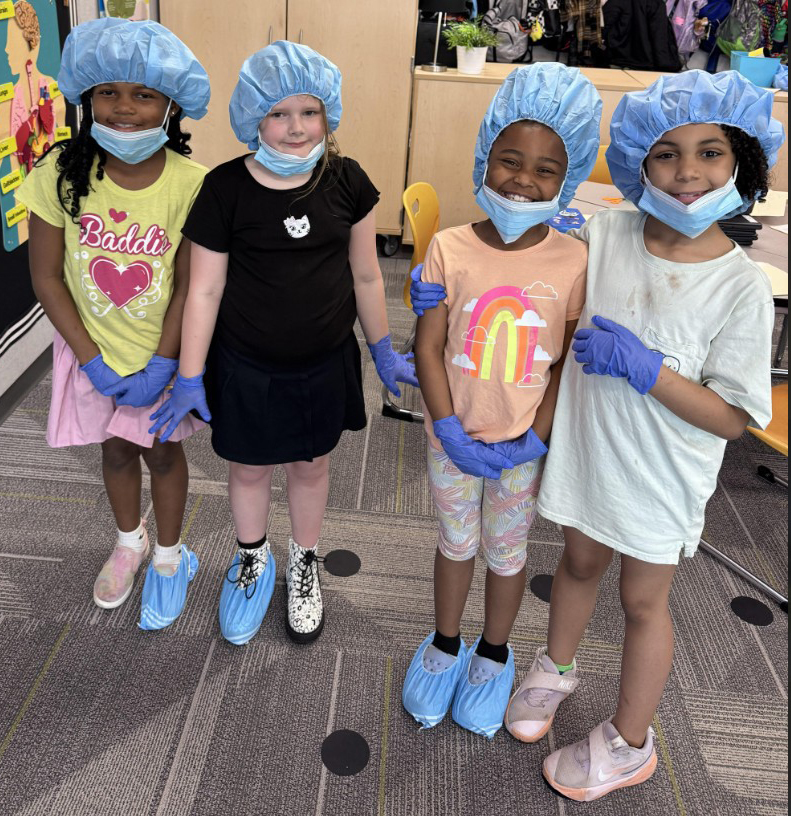 Four girls lined up with surgical hats, masks, and  booties