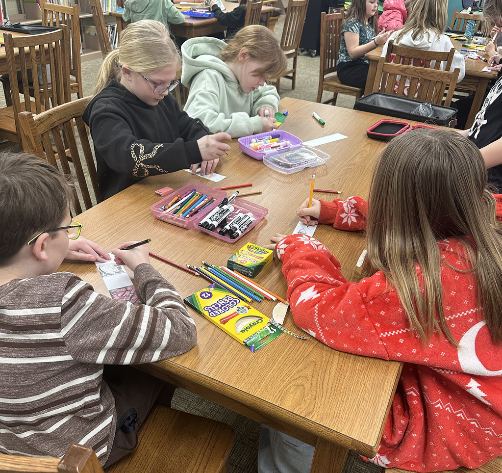 A table of students working on making bookmarks with markers and pencils