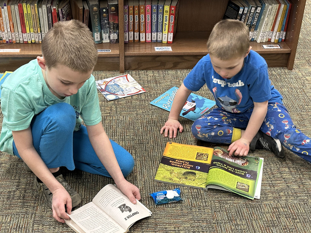 Two elementary boys going through books on the floor of the library