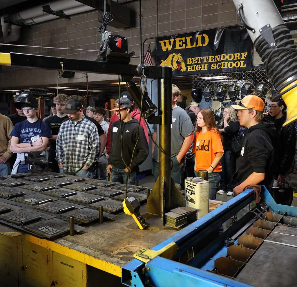 Students gathered around  a table of  metal plates with USA cut into it and wavey lines like a flag next to it an below